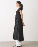 Person in long dress over wide pants, standing sideways in an indoor setting.