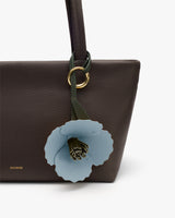 Handbag with flower charm attached to the strap.