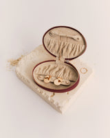 Small jewelry case open on textured surface with rings and earring holders inside.