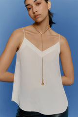 Woman in a sleeveless top with a pendant necklace, posing against a blue background.