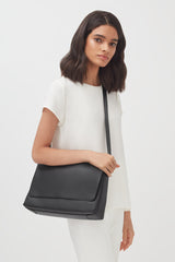 Woman standing with a shoulder bag, looking at the camera.