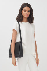 Woman standing, carrying a shoulder bag, looking at the camera.