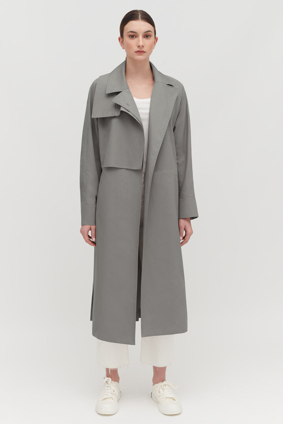Relaxed Trench Person wearing a long coat over a top and pants, standing against a plain background.