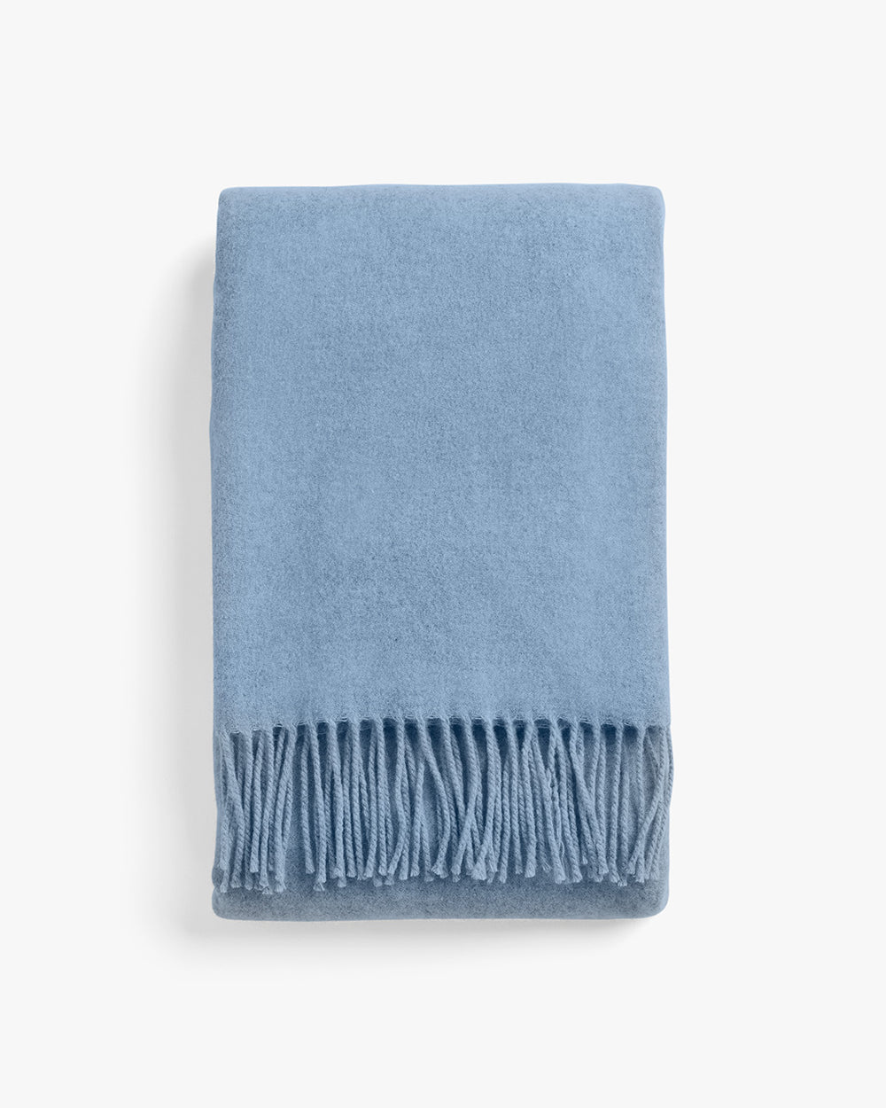 Blanket with fringes folded on a plain background.