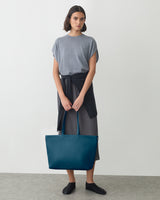 Person holding large tote bag with sweater tied around waist.