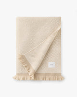 Folded blanket with a fringe detail and a small label.