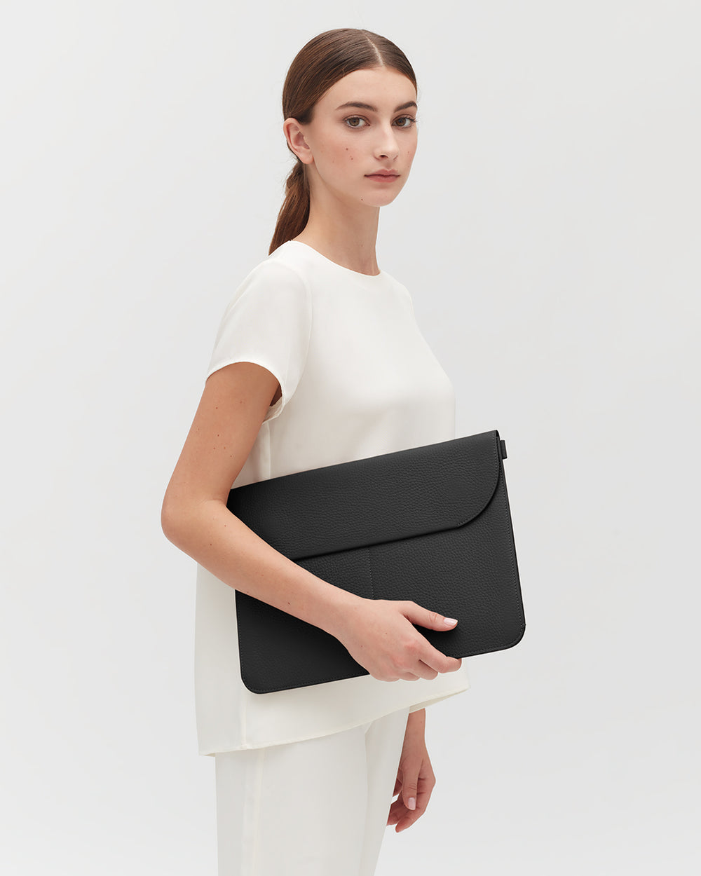 Woman standing holding a large clutch bag.