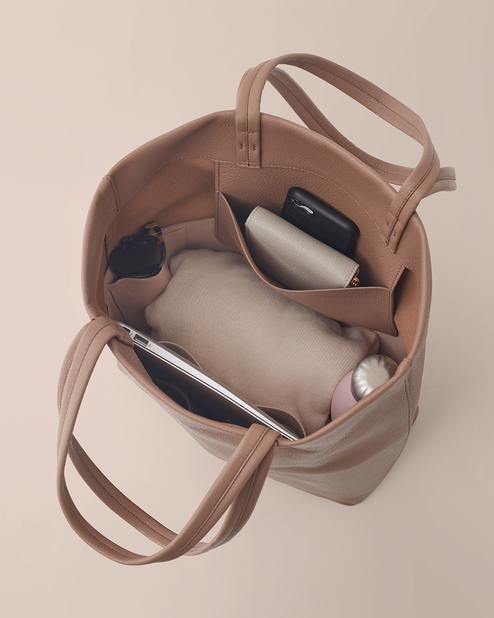 Top view of an open handbag containing a smartphone, sunglasses, and a notebook.