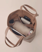 Top view of an open handbag containing a smartphone, sunglasses, and a notebook.