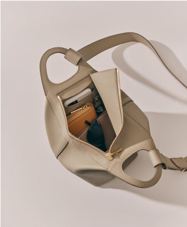 Handbag with an open zipper showing contents, including a wallet, sunglasses, and a phone