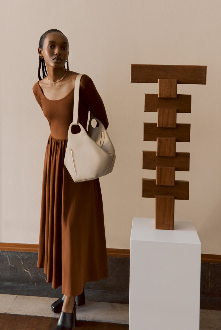 Woman standing next to a sculpture, holding a bag.