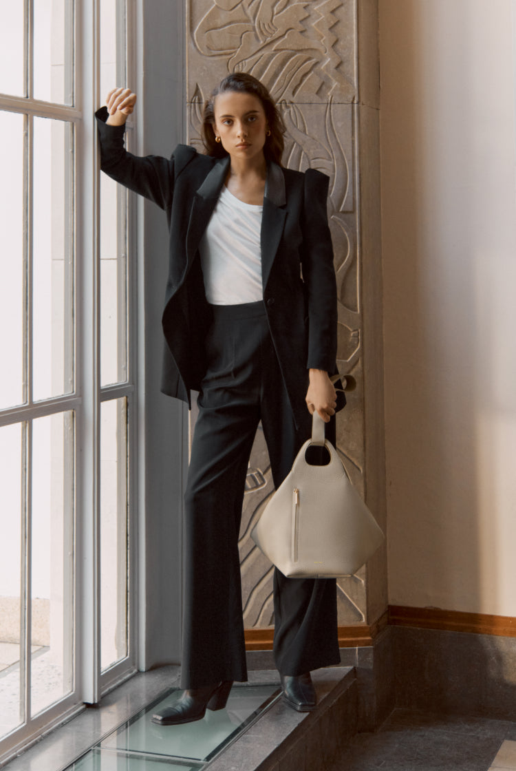 Person in suit standing by a window holding a bag