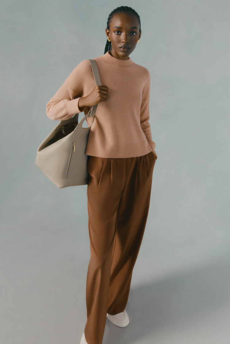 Woman carrying a bag and wearing a sweater and trousers.
