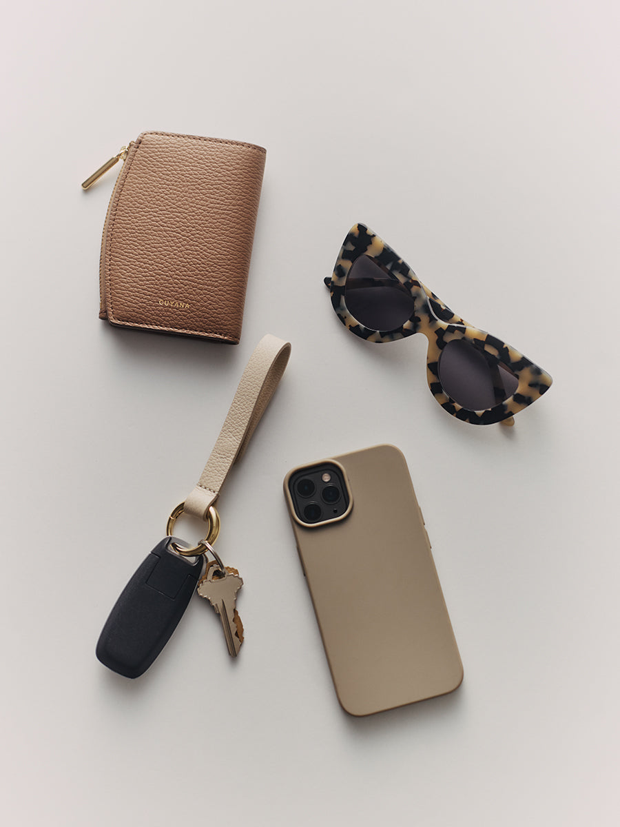 Wallet, sunglasses, phone with case, and key fob with strap on a flat surface.