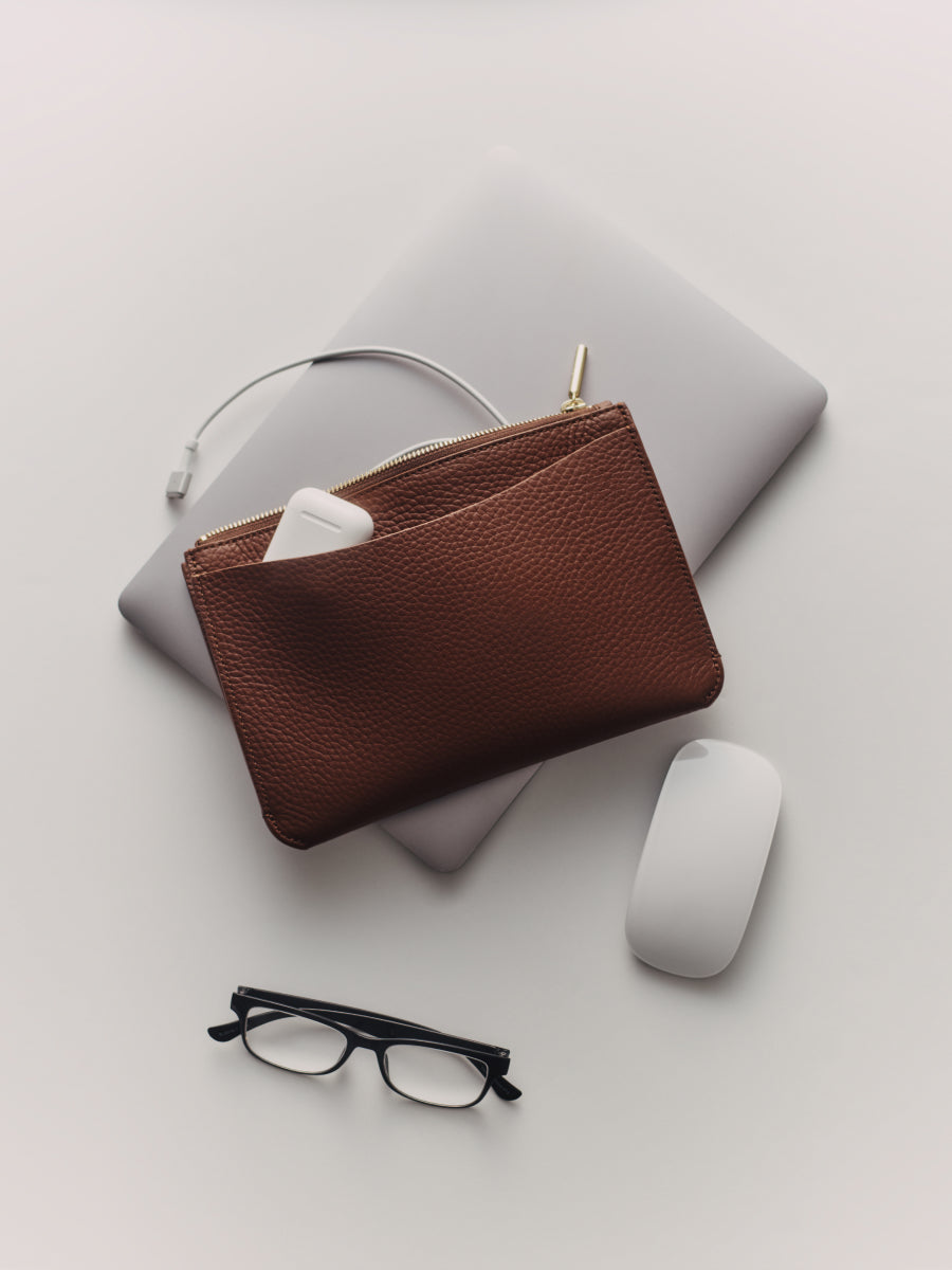 Glasses, a zipper pouch with headphones, laptop, and mouse on a surface.