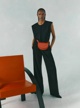 Woman standing next to a chair, wearing a sleeveless top and pants with a waist bag.