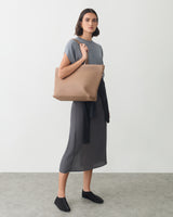 Person standing with a large shoulder bag wearing a long dress and shoes.