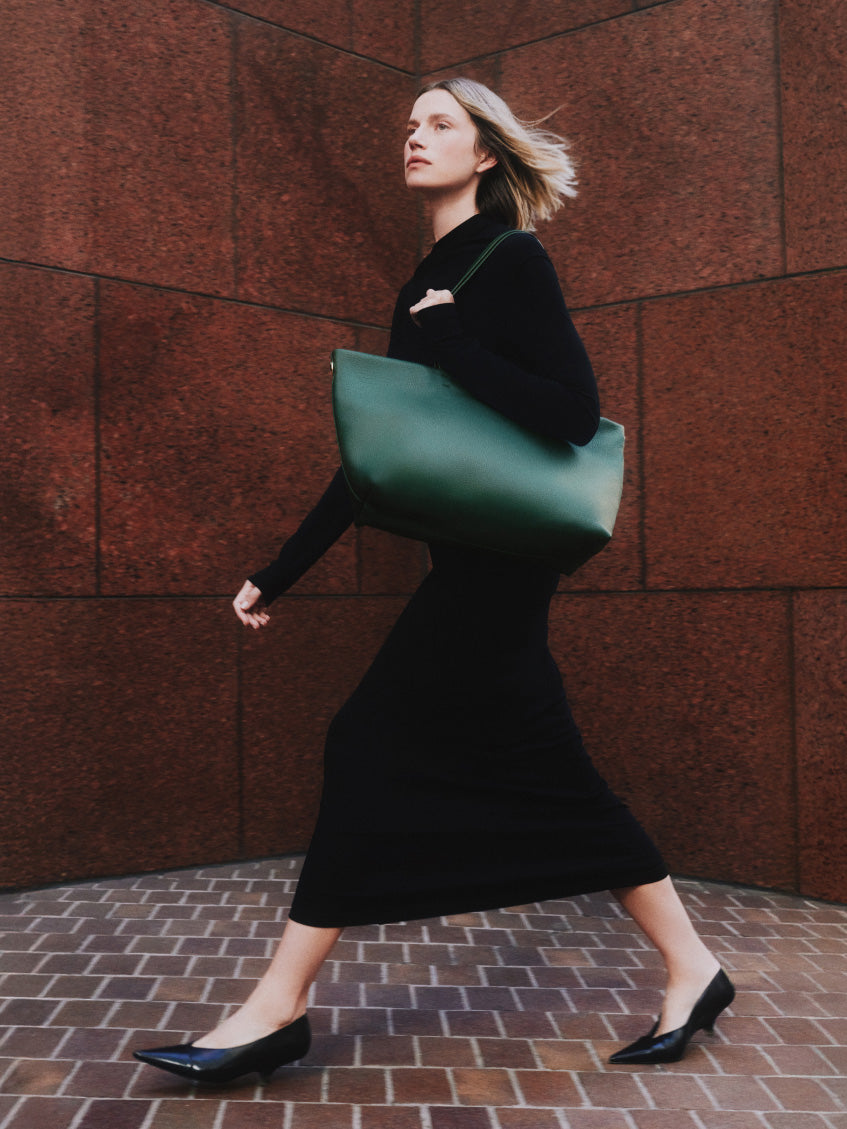 Person walking with large shoulder bag wearing a long dress and shoes.