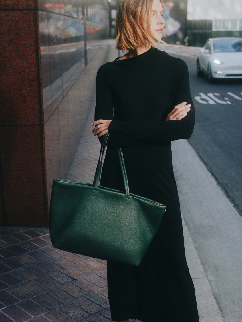 Person in a long dress holding a large handbag on a city street.