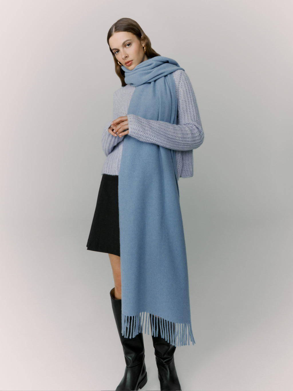 Woman in sweater, skirt, and scarf standing with arms crossed.