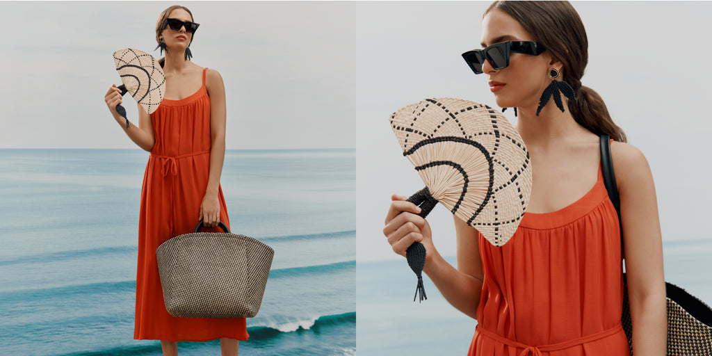 Two women holding fans by the sea, one standing and one closer up.