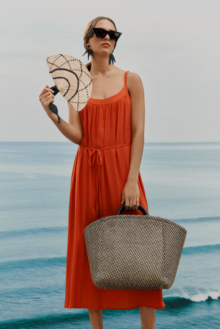 Woman holding a fan and bag standing by the sea