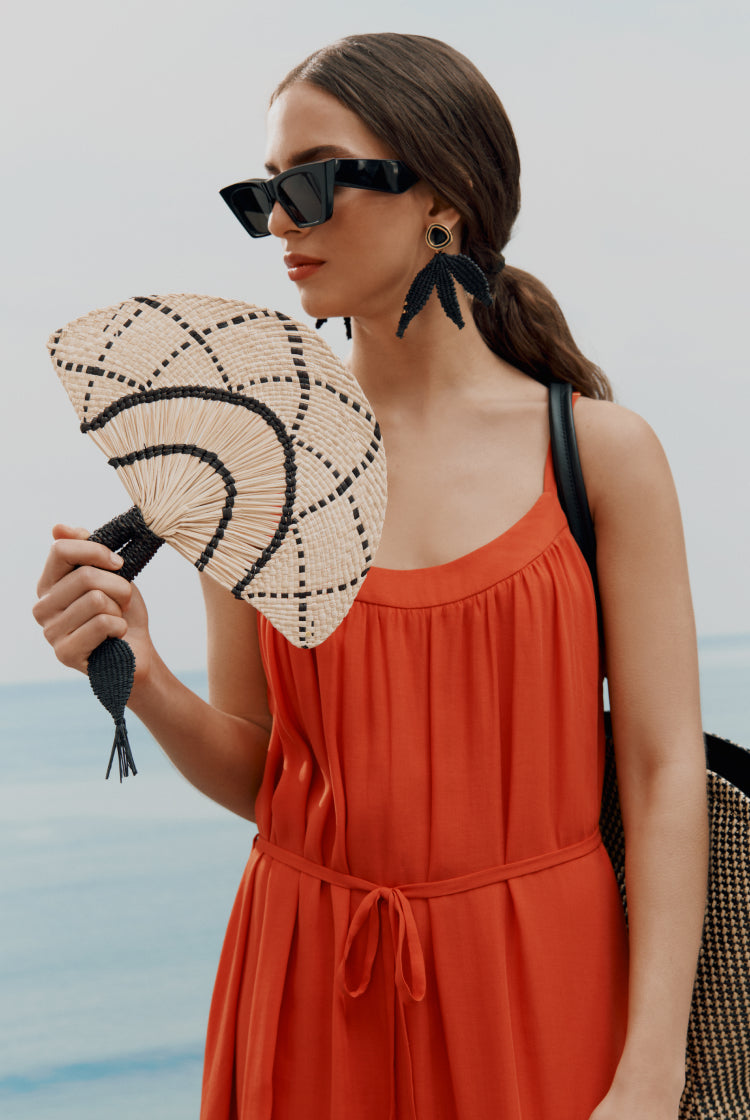 Woman holding a hand fan near the ocean.