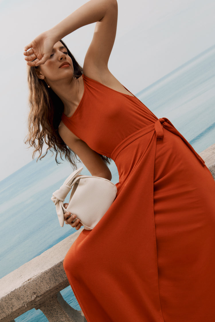Woman in a dress posing by the sea with a handbag.