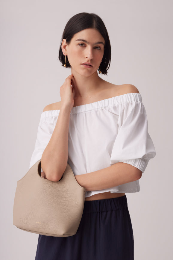 Model in white top and navy pants holds a small beige handbag. 