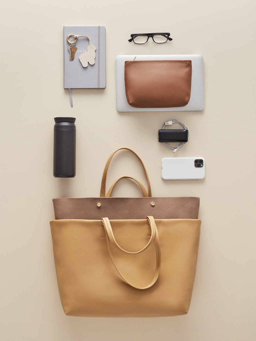 Arranged items including a tote bag, notebook, keys, glasses, clutch, bottle, watch, and smartphone.