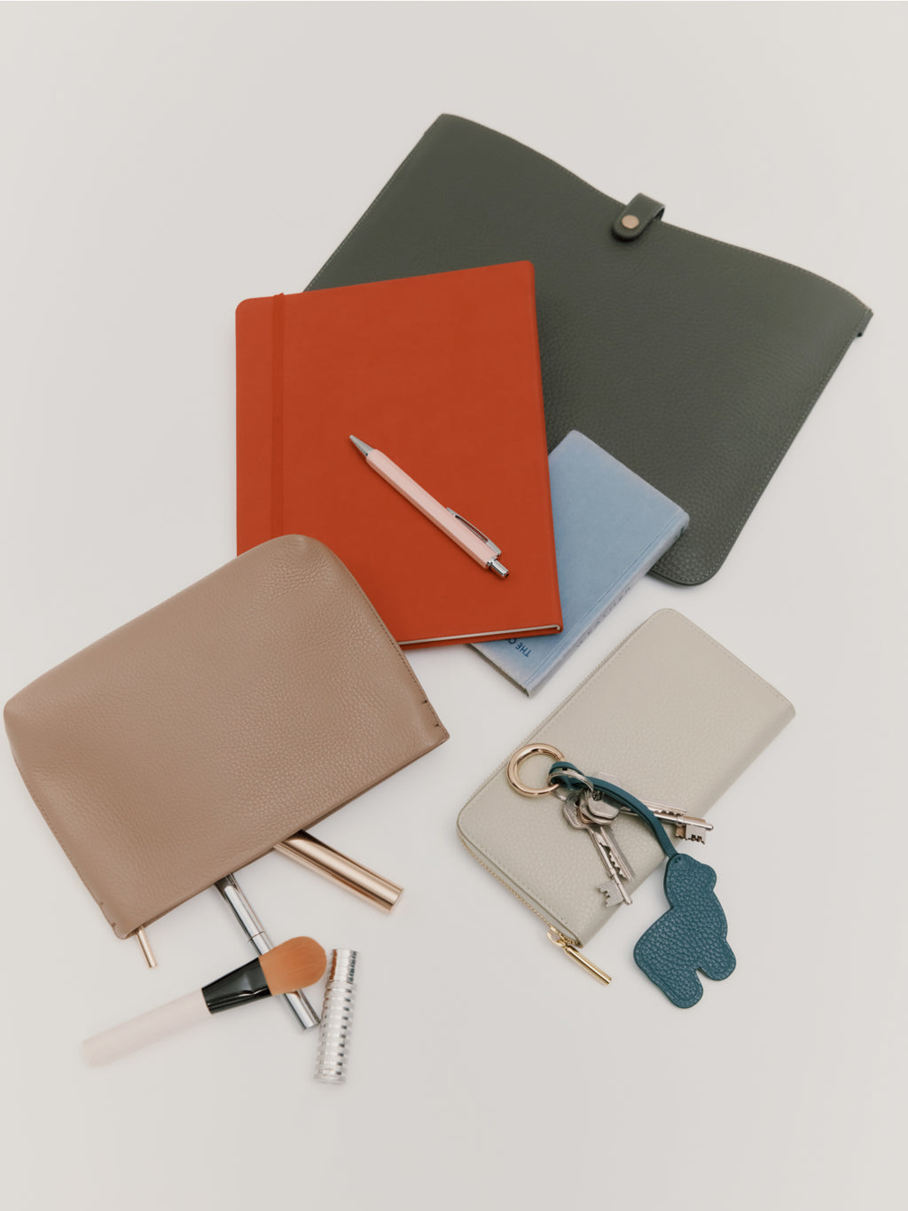 Various notebooks, a pen, a pouch, makeup items, and keys arranged on a surface.