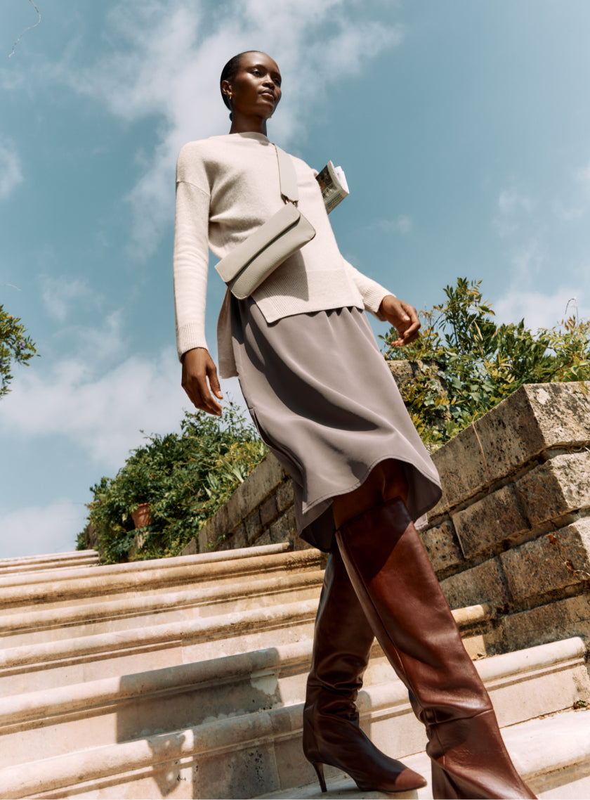 Woman walking down stone steps in stylish outfit and tall boots.