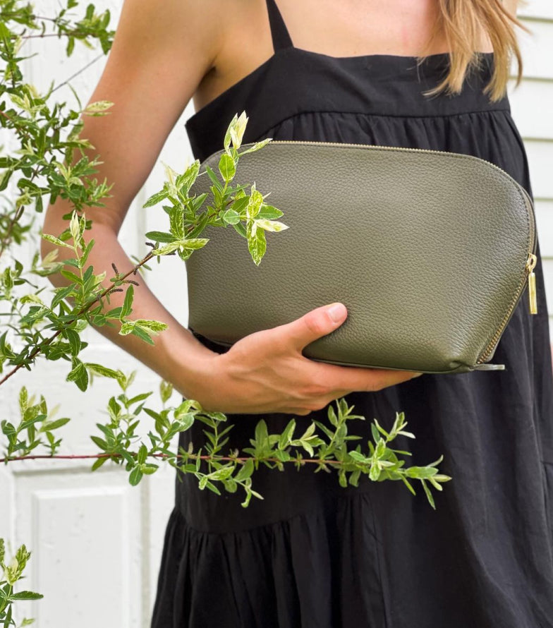 Woman holding a purse near green foliage.