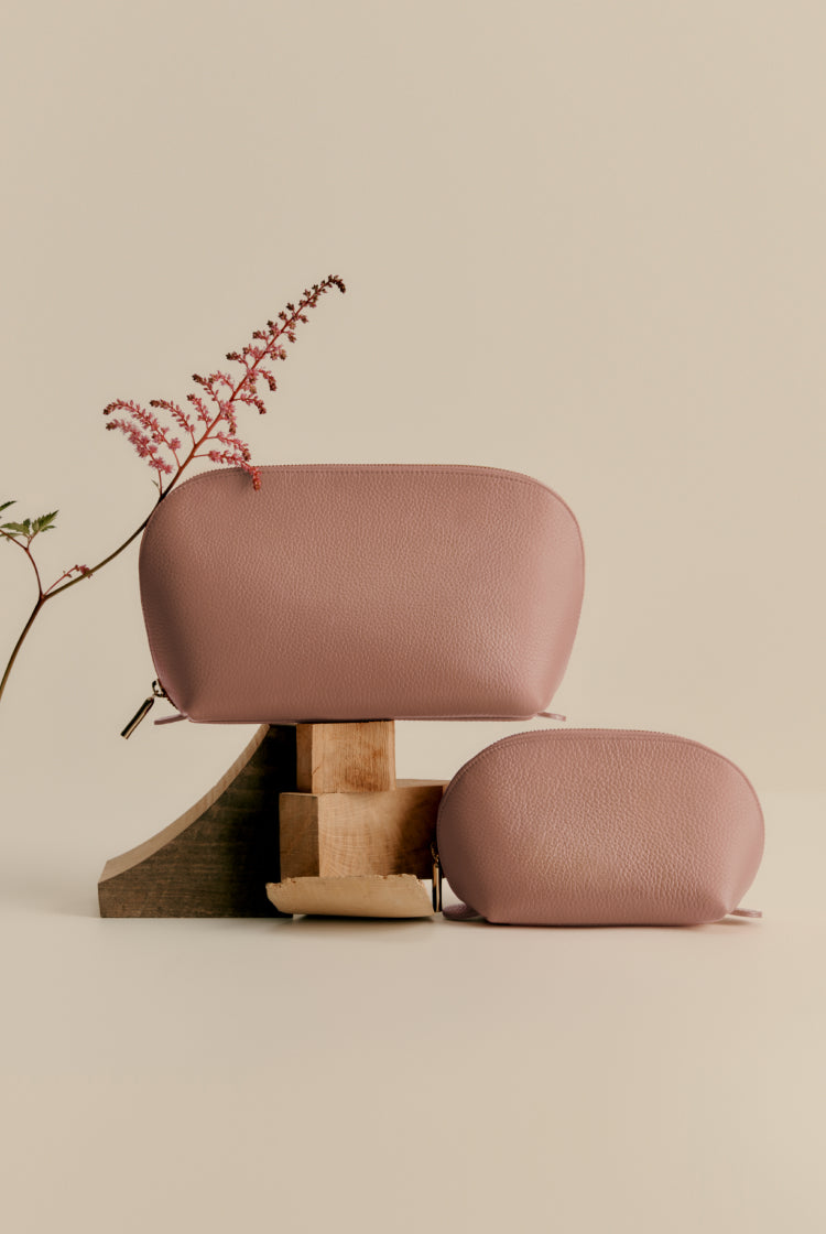 Two handbags on a wooden stand with a floral twig next to it.