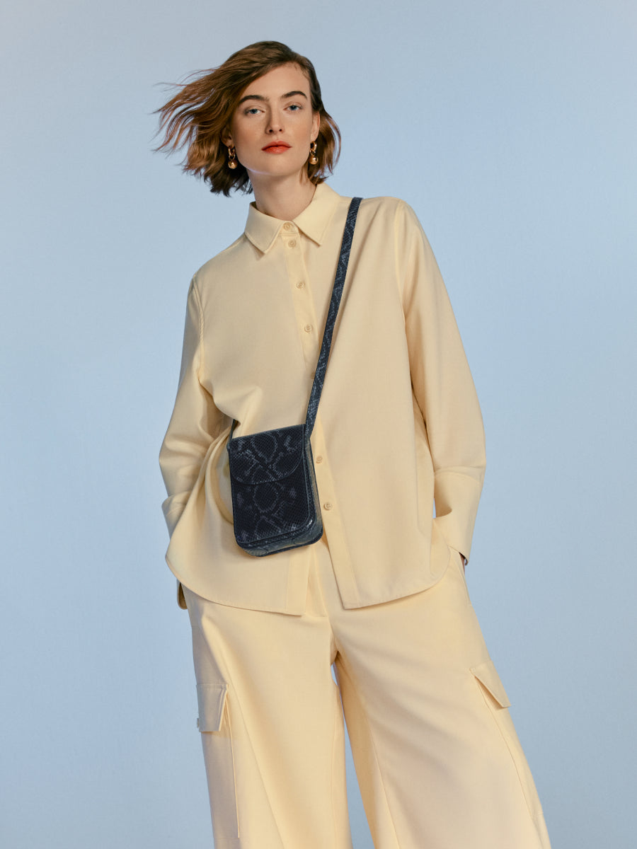 Woman in elegant outfit with small shoulder bag, standing.