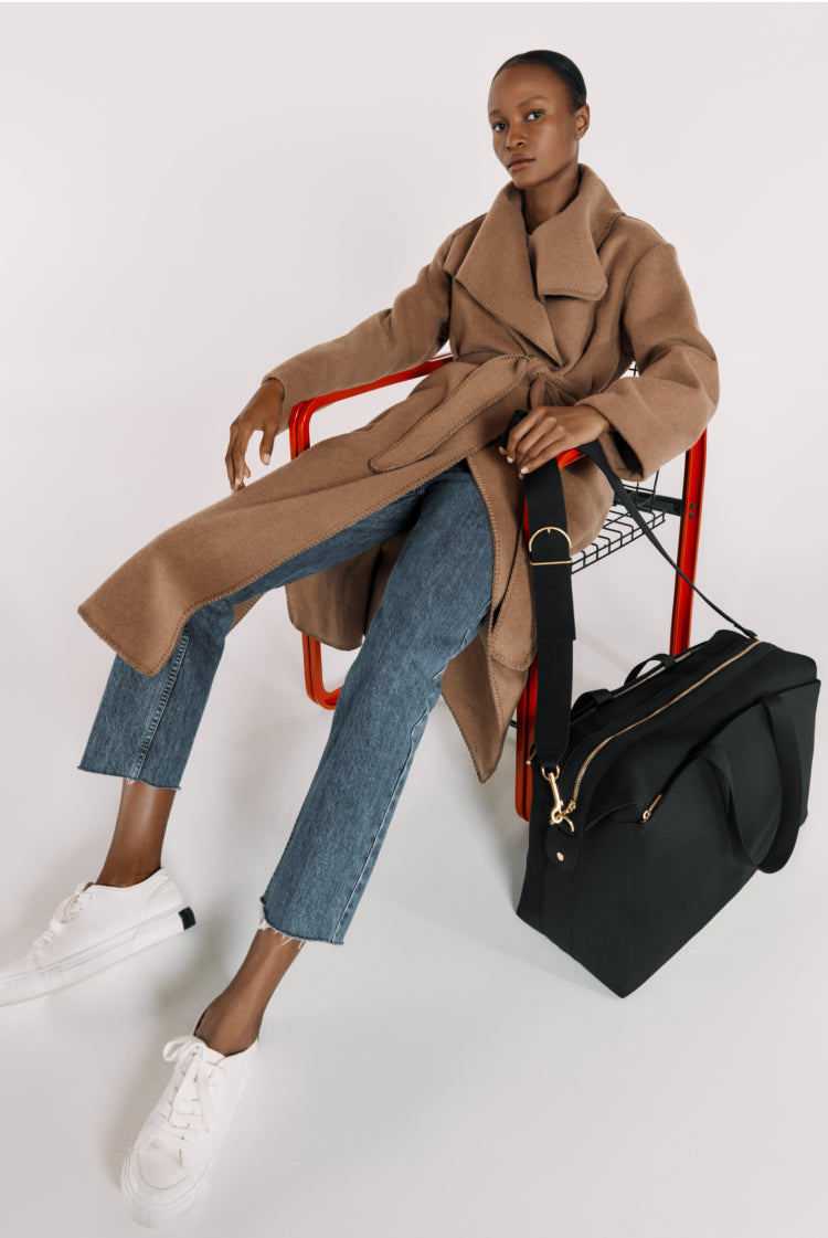 Woman sitting on red chair with a large bag next to her.