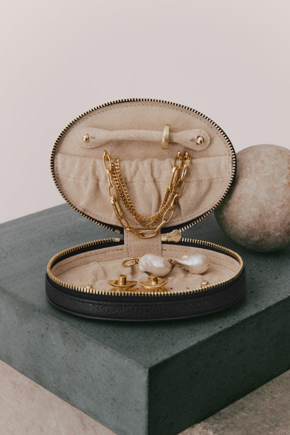Jewelry case open with necklace and earrings inside, placed on a pedestal.