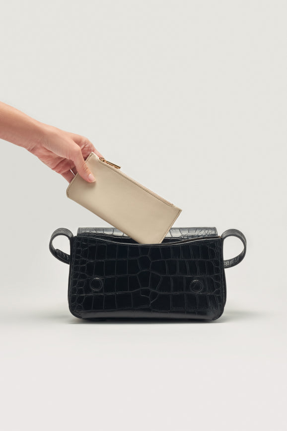 Hand placing a wallet into an open handbag on a plain background.