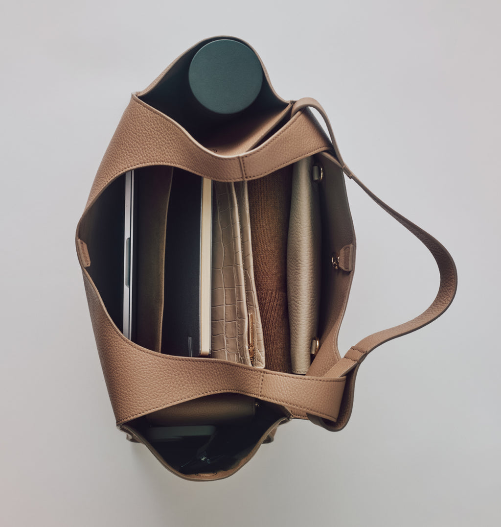 Top view of a tote bag containing a water bottle, a croc-embossed leather wallet, and a few other items