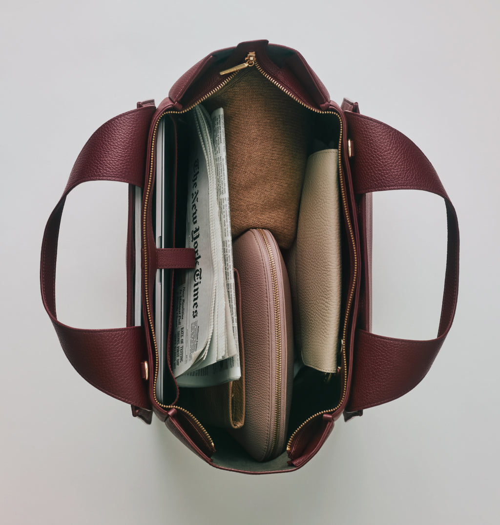 Open travel bag with newspaper, clothes, and pouches inside.