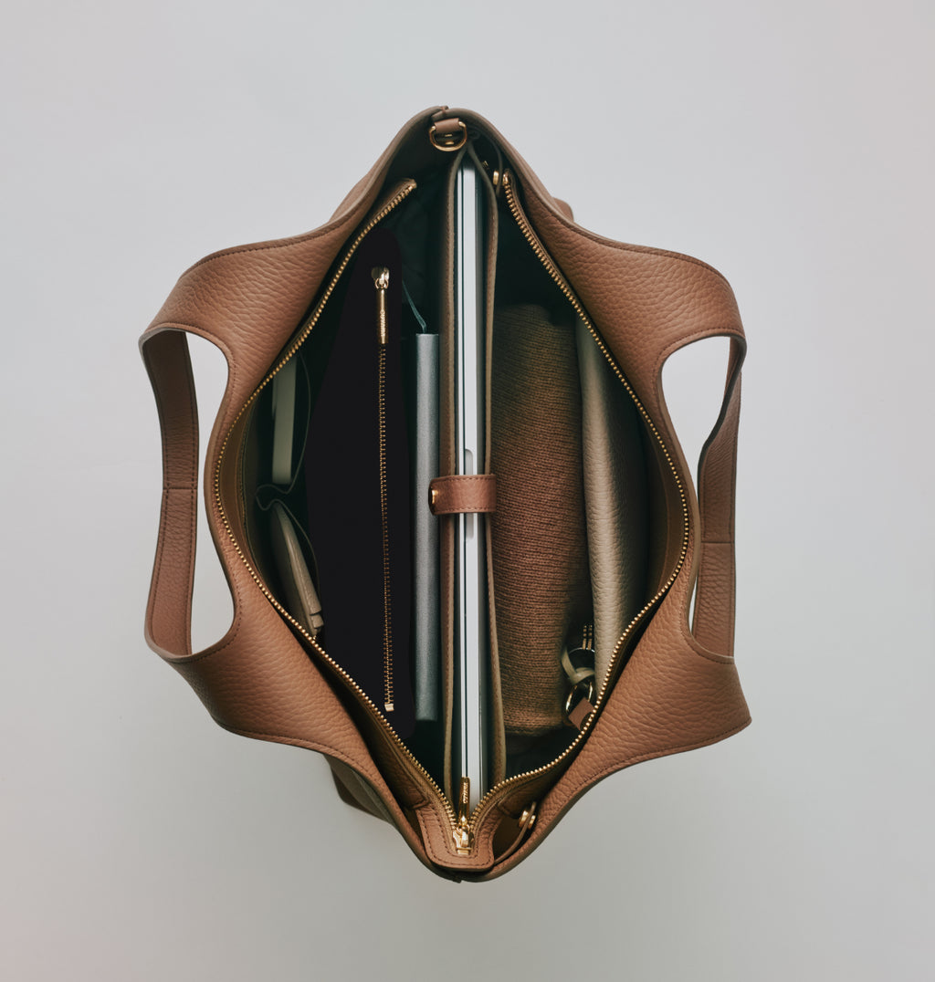 Open tote bag with two handles showing contents including a laptop, notebook, and a zipper pocket