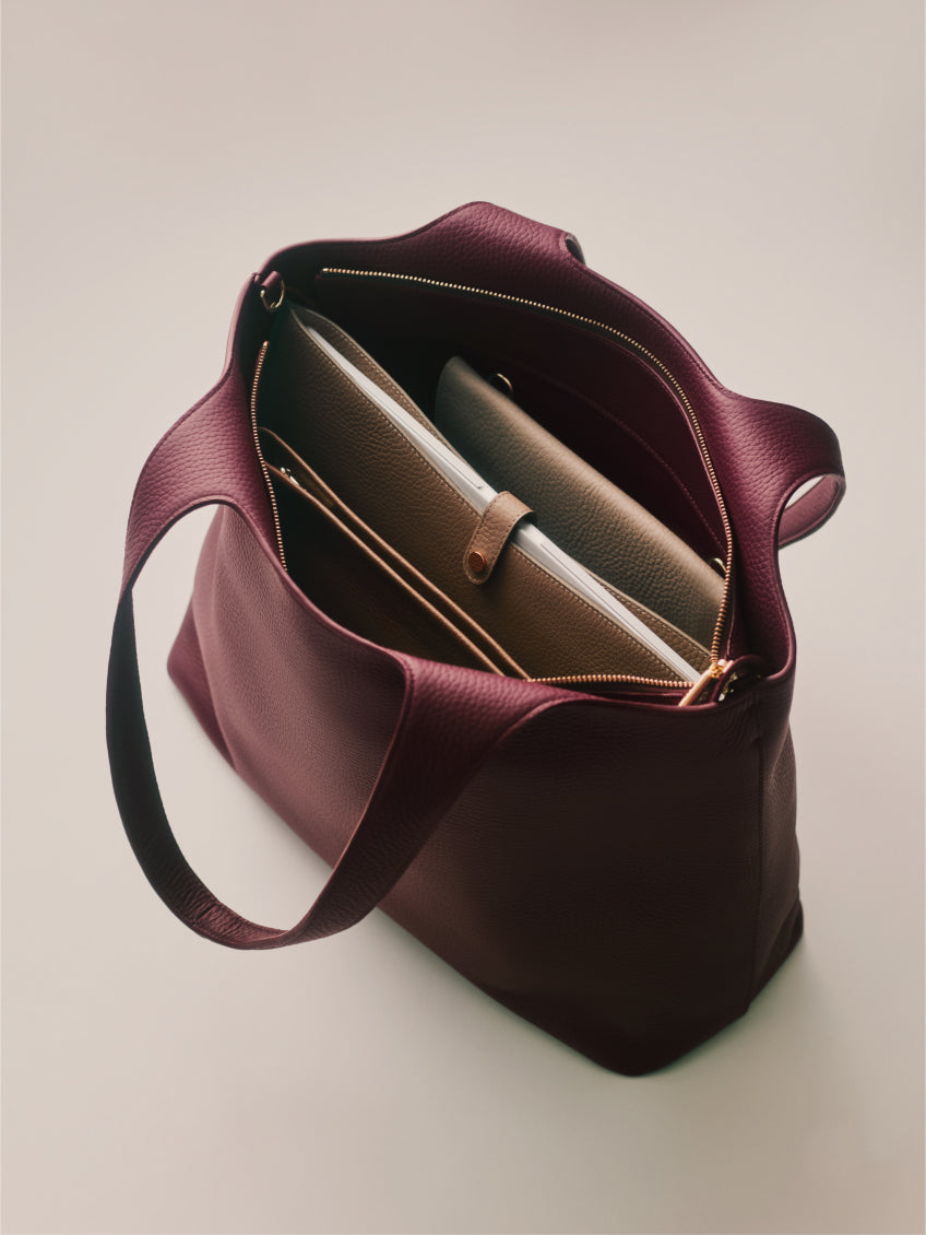 Open handbag with contents organized in multiple compartments, including a tablet and zippered pouch