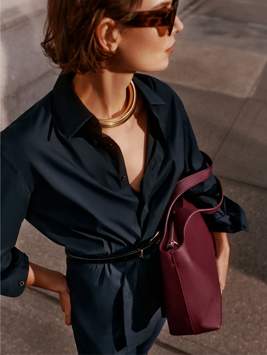Person wearing a collared shirt, gold necklace, sunglasses, holding a bag on the shoulder