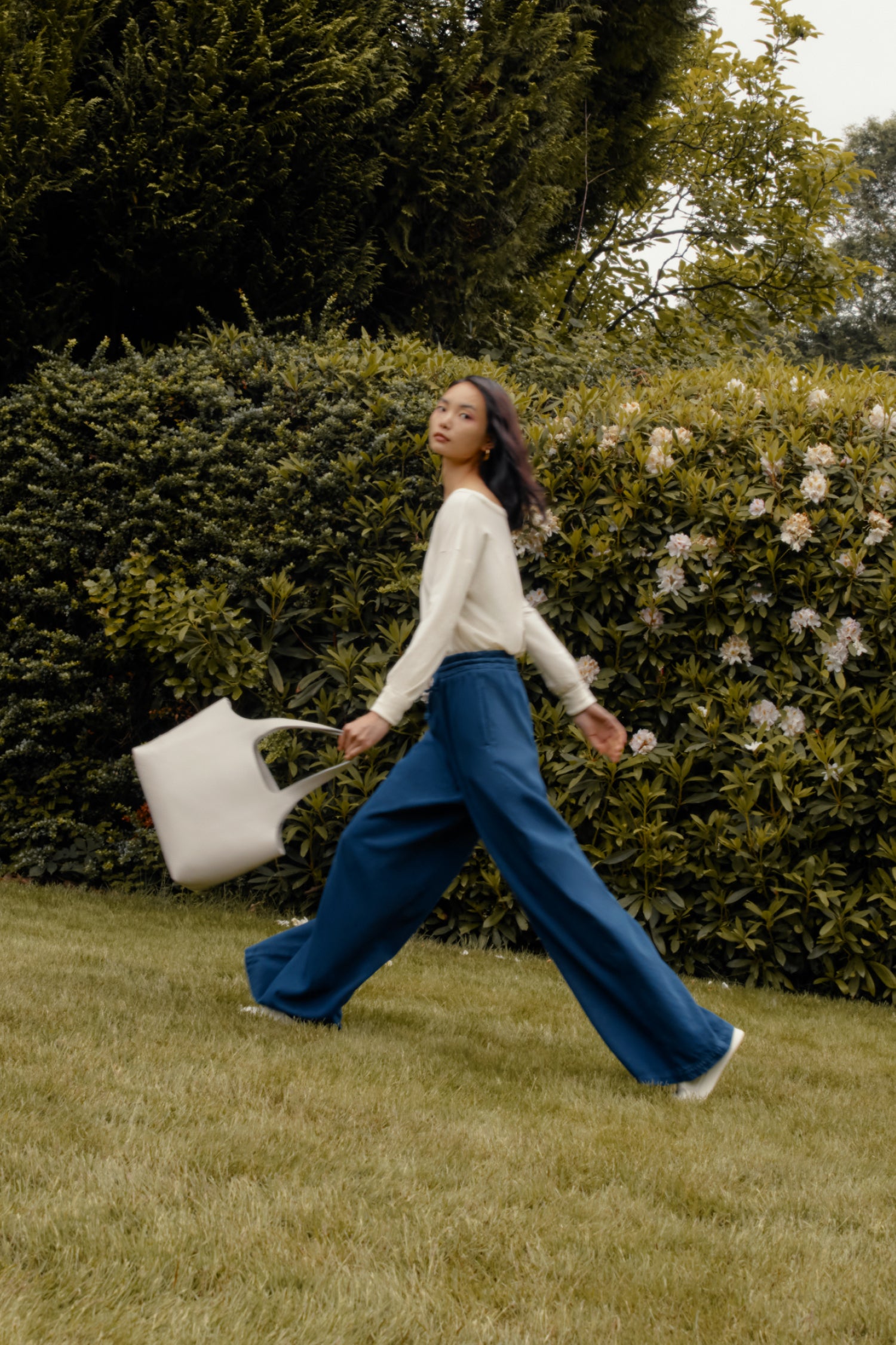 Woman walking in a garden holding a watering can.