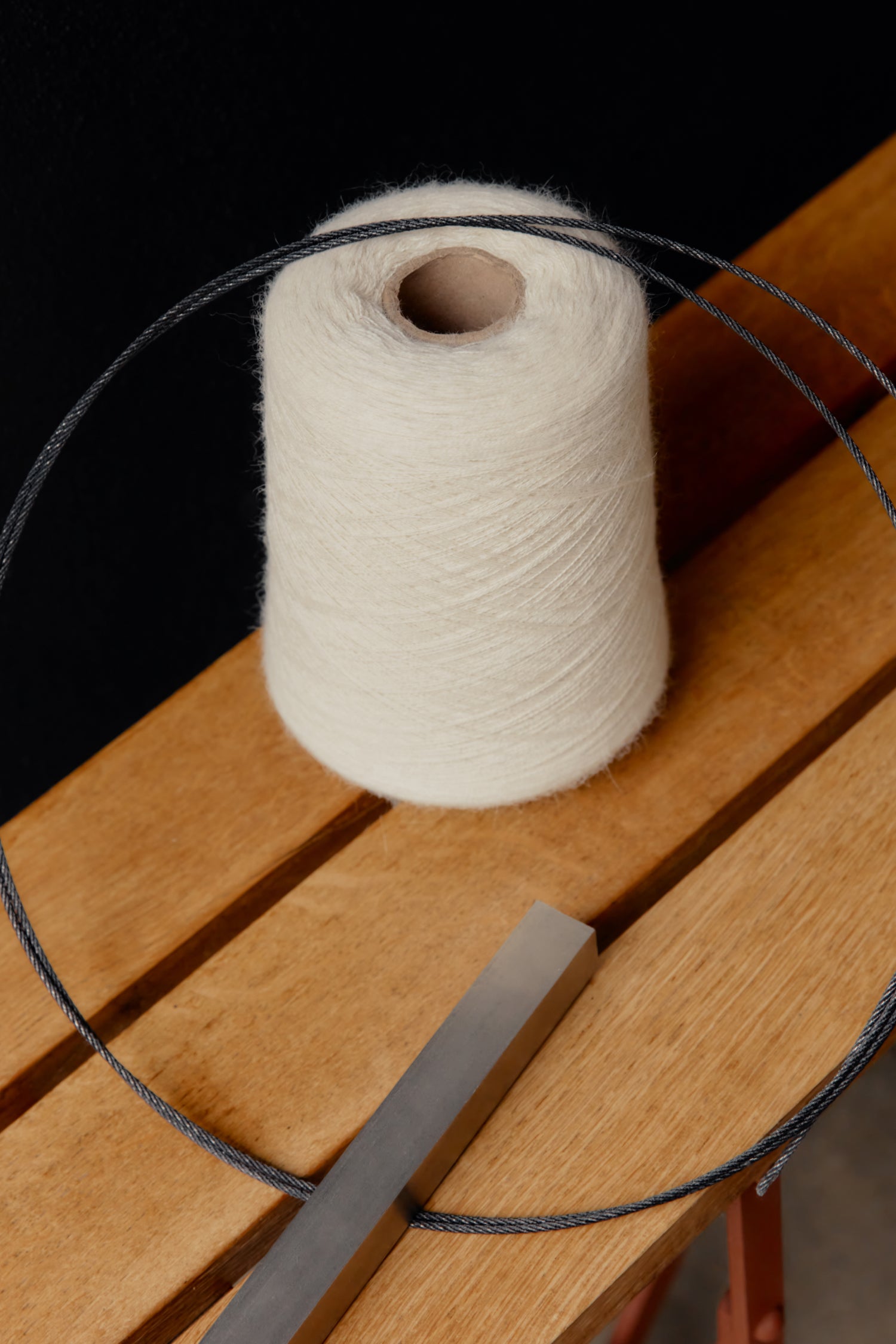 Yarn spool on a wooden chair with a metal rod and string looped around it.