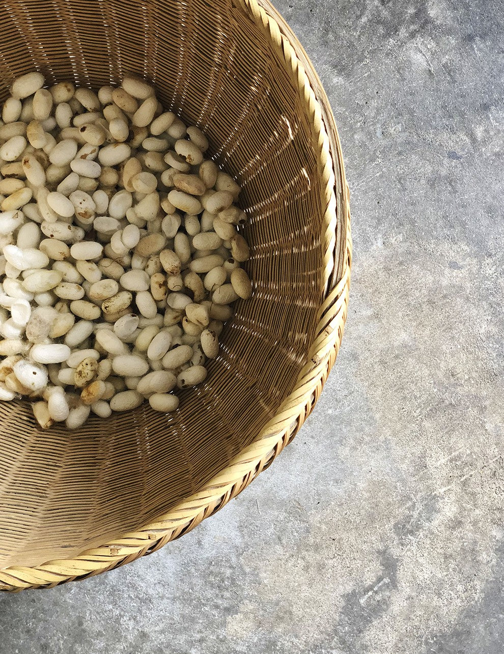 Top view of a basket filled with beans placed on a textured surface.