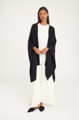 Woman standing in a studio wearing a draped top, wide-leg pants, and flats.