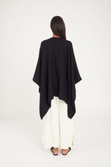 Woman from behind wearing a cape and wide-leg pants, standing in studio.