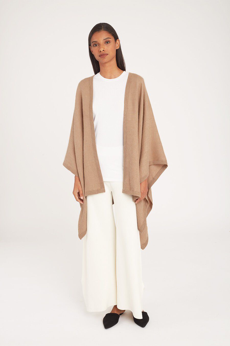 Woman standing in a cape over a top and wide-leg pants.
