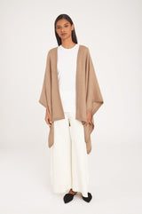 Woman standing in a cape over a top and wide-leg pants.